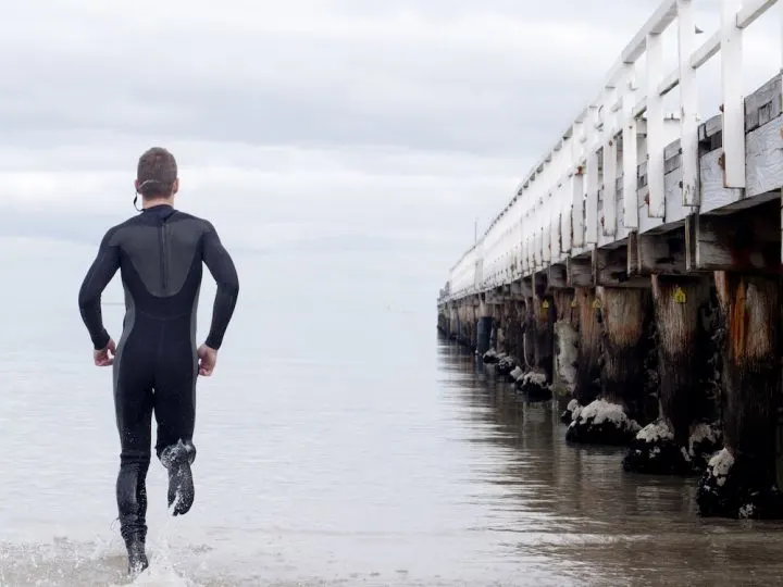 man running to water with wet suit