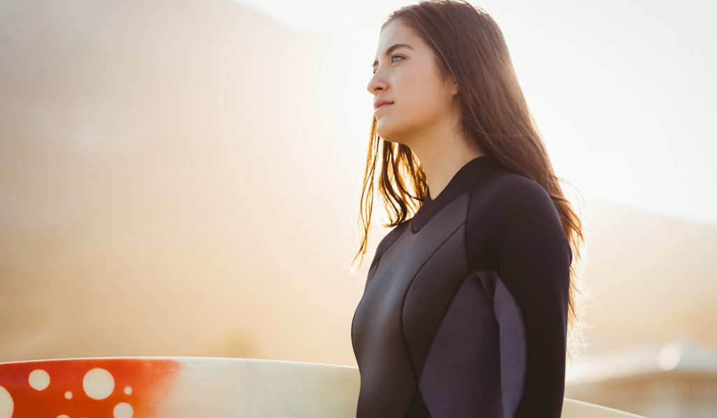 woman in a surfing wet suit holding a surf board