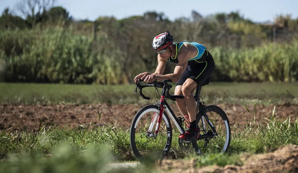 Man riding his triathlon  bike in a road surrounded by fields 