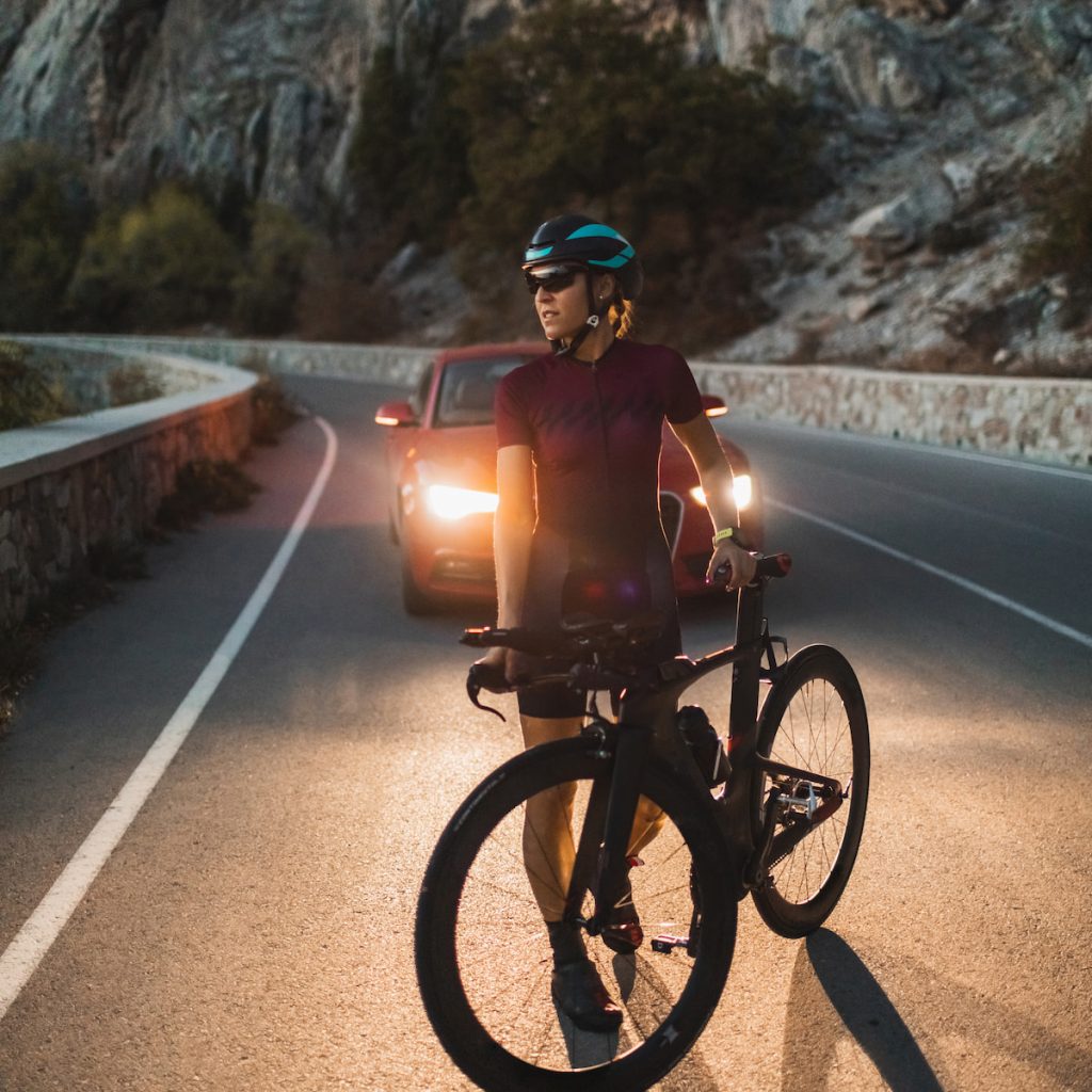 Portrait of cyclist woman with road triathlon bike in headlights of car in twilight 