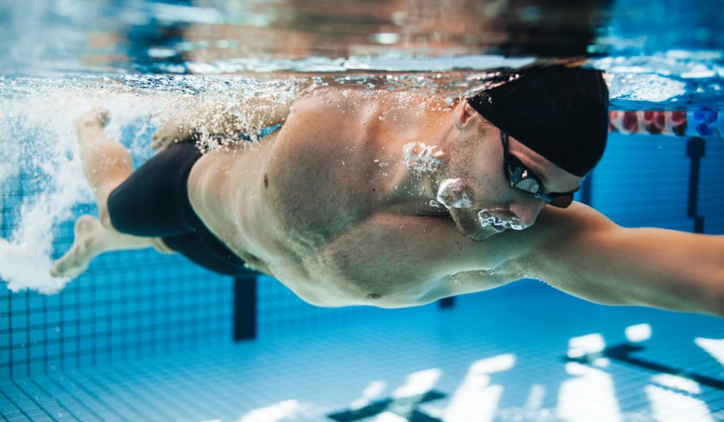 Professional male swimmer swimming in pool wearing swim cap