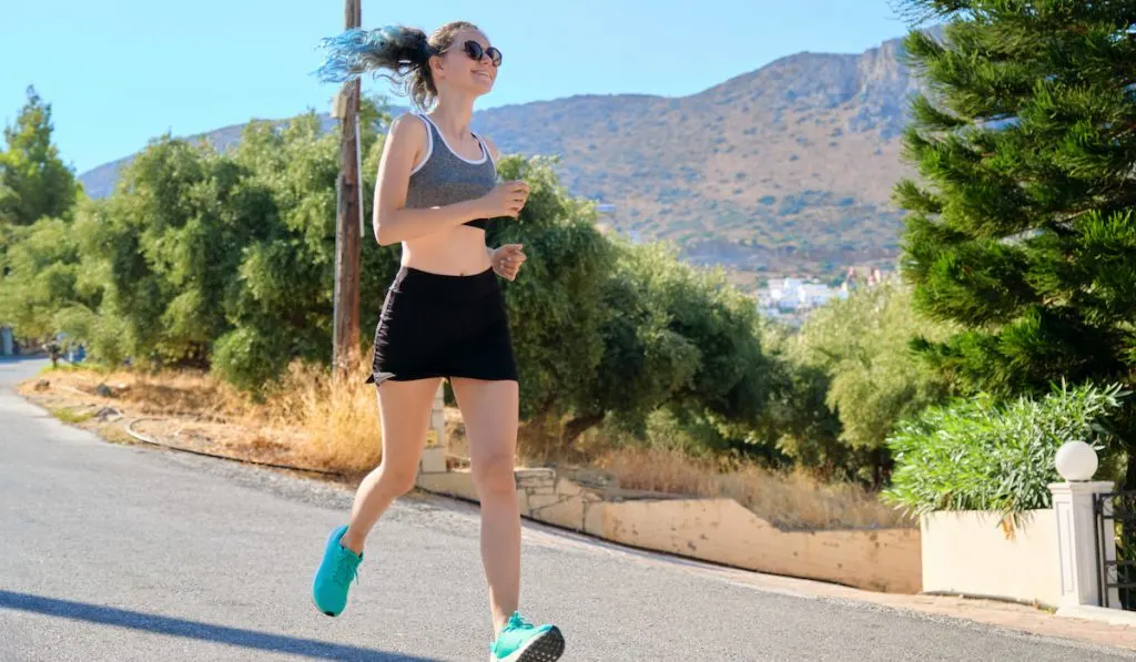 Smiling Girl teenager runner, female running on mountain road 