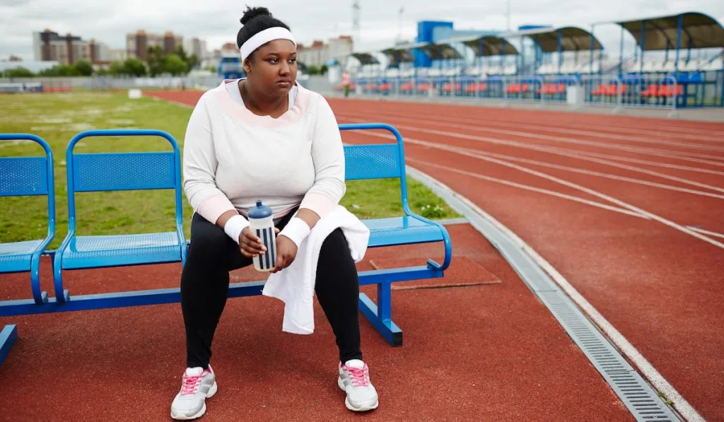 Tired runner resting on a bench with drinking bottle