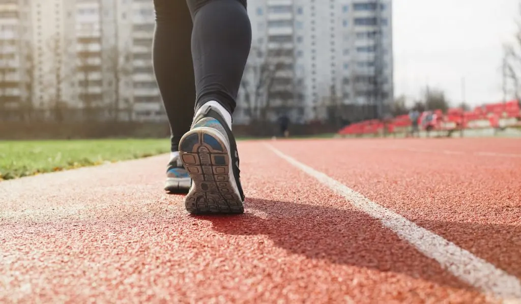 Woman runner sprinting on a treadmill in a stadium, outdoors. Close-up of female legs in sports