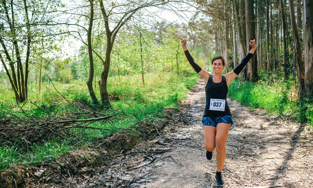 Happy Young woman winning trail race in the forest
