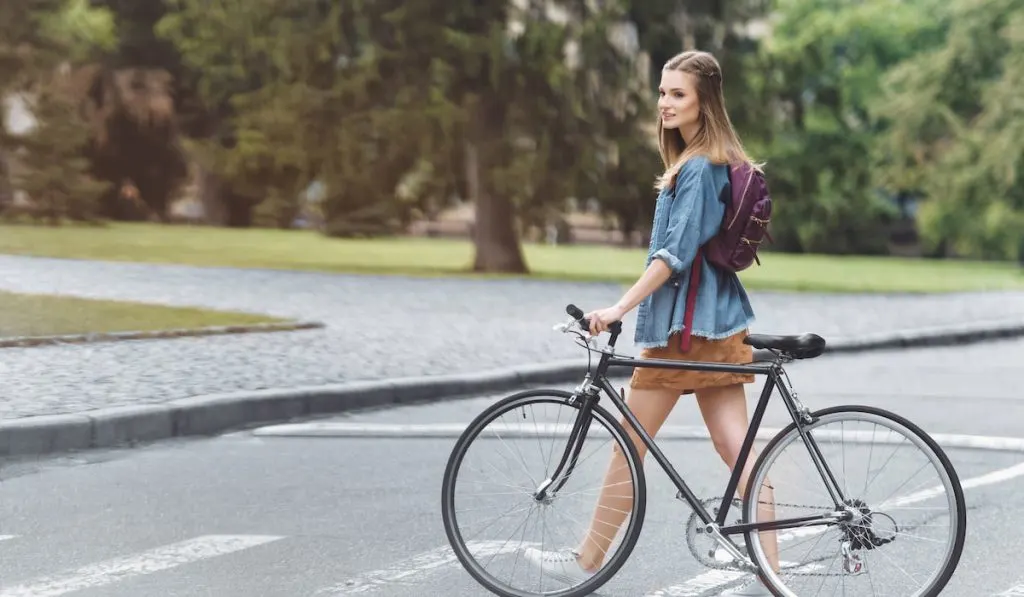 happy beautiful girl with bicycle passing the road in park
