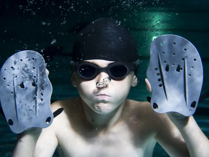 Little-boy-underwater-the-pool-with-swimming-hand-paddles