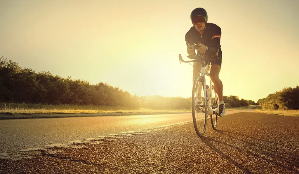 Cyclist riding his bike with aero bars on highway during sunset