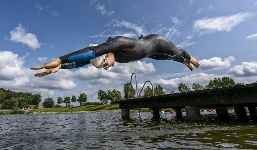 Young female triathlete jumping into a lake
