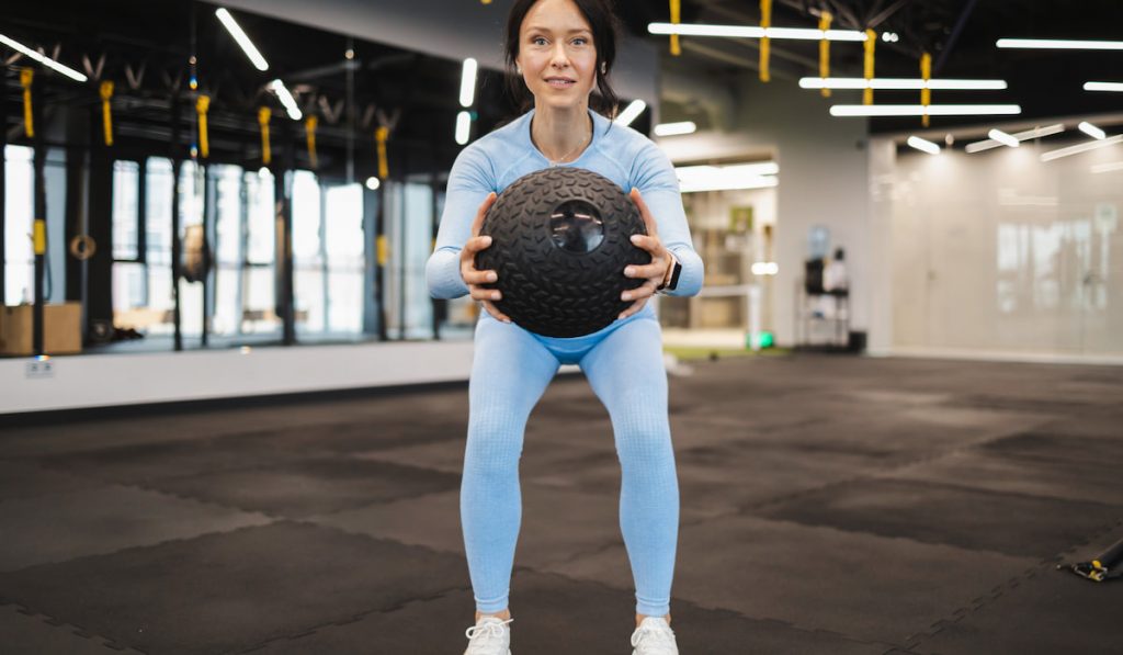 woman doing squat with medicine ball at gym